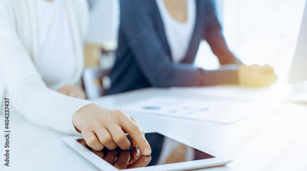 Businesswoman pointing at tablet computer screen while giving presentation to her female colleague. Group of business people working at the desk in office. Teamwork concept Businesswoman pointing at tablet computer screen while giving presentation to her female colleague. Group of business people working at the desk in office. Teamwork concept