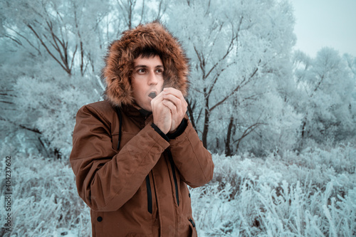 Valokuva A man freezes in the cold in the forest and tries to wipe his hands with his breath