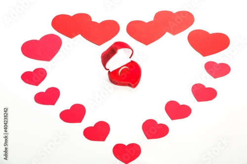 A large heart made of paper hearts laid out on a white background in the middle of a box with a ring.