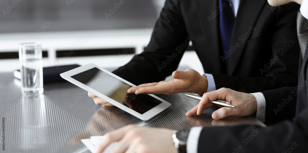 Unknown businessmen using tablet computer and work together at the glass desk in modern office, close-up. Teamwork and partnership concept Unknown businessmen using tablet computer and work together at the glass desk in modern office, close-up. Teamwork and partnership concept