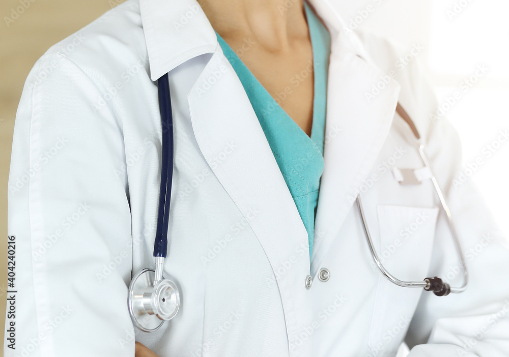 Unknown female doctor standing with stethoscope in sunny clinic, close-up Unknown female doctor standing with stethoscope in sunny clinic, close-up