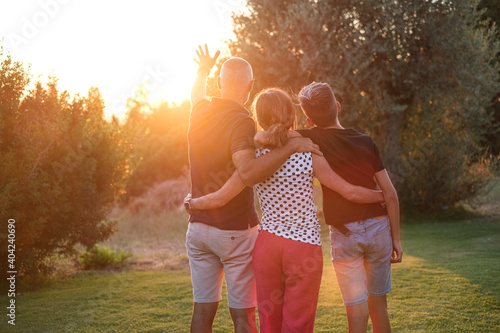 Famiglia composta da tre persone , di spalle ,si abbraccia in segno di unione rivolti verso il tramonto in un contesto naturale photo