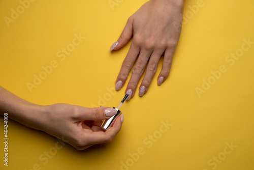 Close-up of a woman paints her nails with lacquer on a yellow background, top view