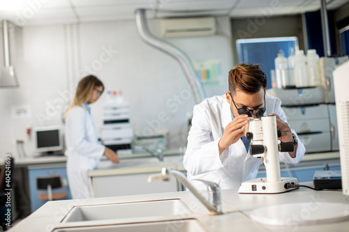 Young scientist in white lab coat working with binocular microscope in the material science lab