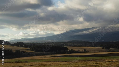 Timelapse of clouds over landscape under High Tatras rocky mountains in windy winter day, Slovakia. Landscape of fields, meadows and forest under mountains not covered with snow due to climate changes
