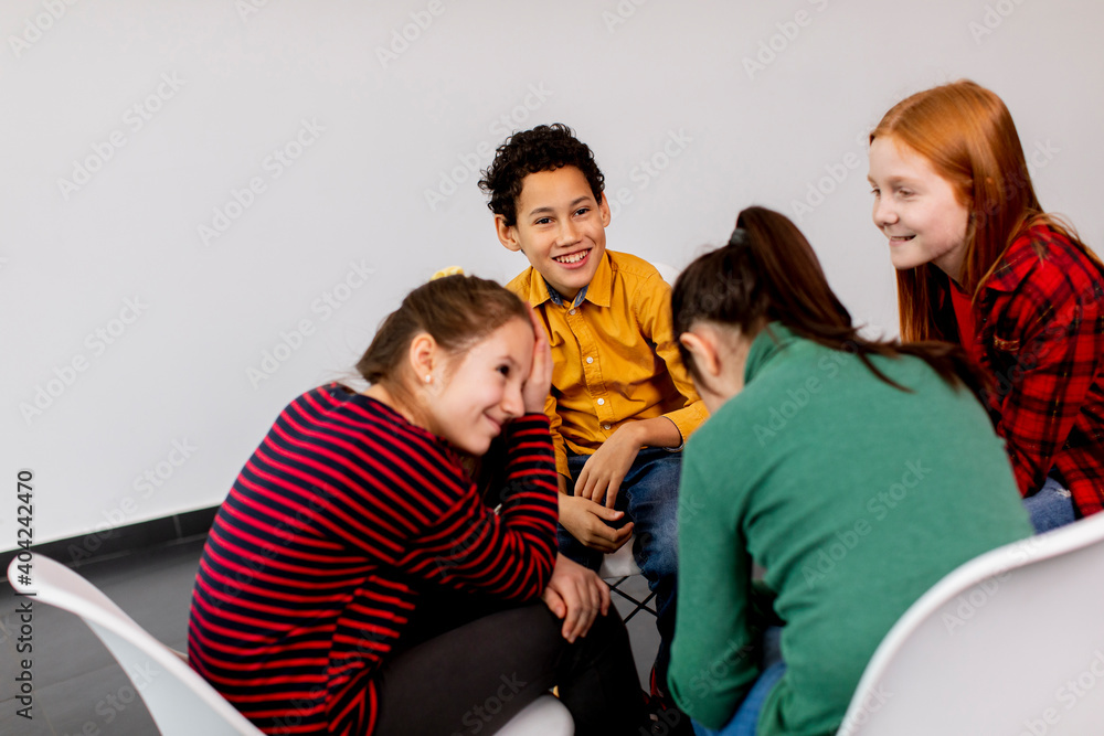 Portrait of cute little kids in jeans  talking and sitting in chairs against white wall