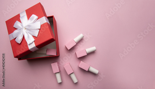 Open red gift box with gel polishes on pink background