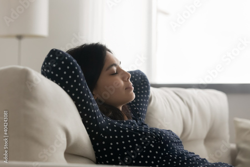 Side view relaxed young asian korean woman daydreaming napping leaning on comfortable couch, enjoying peaceful stress free lazy leisure weekend time in living room, meditating with close eyes.