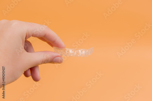 Dental retainer in hand on orange background. Orthodontics. Dental tray. Place for inscription