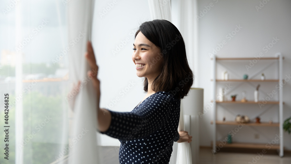 Side view happy millennial asian korean woman opening curtains, admiring morning cityscape view, smiling beautiful lady enjoying peaceful morning time, woke up early on weekend starting new day. Side view happy millennial asian korean woman opening curtains, admiring morning cityscape view, smiling beautiful lady enjoying peaceful morning time, woke up early on weekend starting new day.