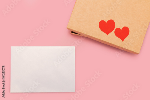 closed gift box and two paper hearts on it isolated on pink background