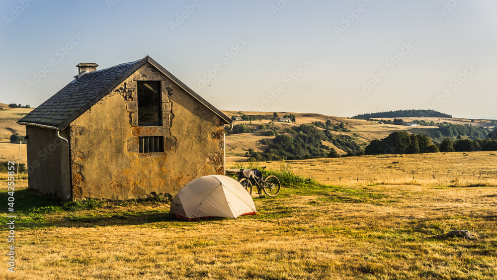 Tent and bicycle near an old herdsman's hut at sunrise in Auvergne, France