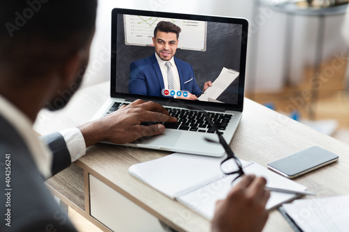 Black businessman video calling business partner on laptop at workplace