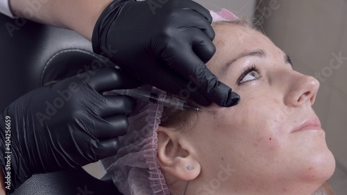Young woman getting beauty facial injections in salon. Beautician in protective medical mask makes cosmetic injection into the patient face. Beauty injections, mesotherapy and revitalization