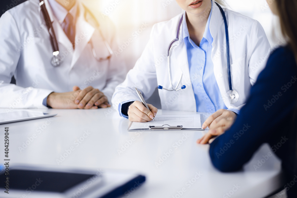 Unknown woman-doctor with male colleague are consulting patient woman while sitting at the desk in modern clinic, close-up. Perfect medical service, medicine concept Unknown woman-doctor with male colleague are consulting patient woman while sitting at the desk in modern clinic, close-up. Perfect medical service, medicine concept