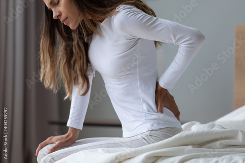 Fotografie Close up unhappy woman wearing pajama rubbing stiff back muscles after awakening
