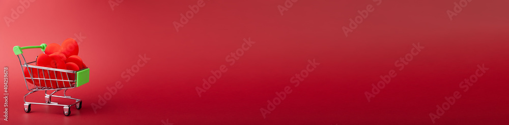 Banner with Red hearts inside mini grocery cart, shopping bucket on red background Banner with Red hearts inside mini grocery cart, shopping bucket on red background