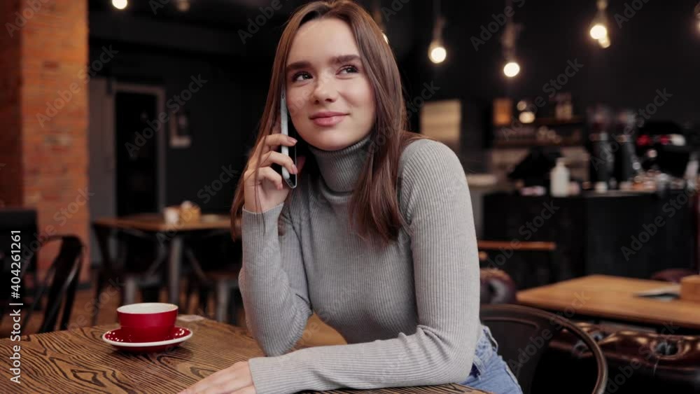 Beautiful young woman speaking on mobile phone sitting in coffee shop. Close up portrait of smiling girl talking smartphone with colleagues, friends or relatives. Beautiful female freelancer Beautiful young woman speaking on mobile phone sitting in coffee shop. Close up portrait of smiling girl talking smartphone with colleagues, friends or relatives. Beautiful female freelancer