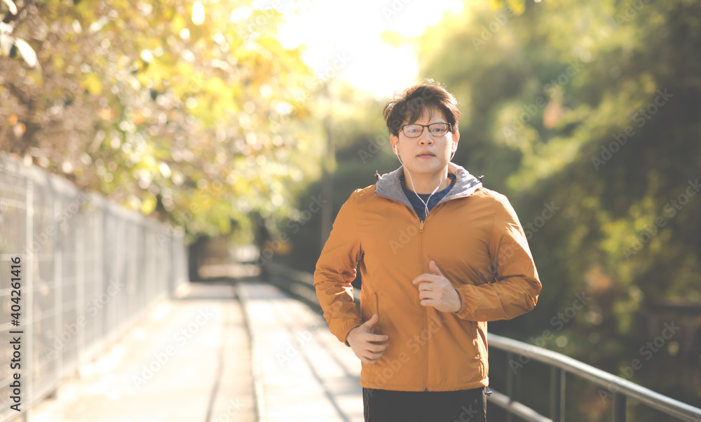 Obraz premium Asian Man in yellow hoodie jogging and running beside road in park at autumn morning.
