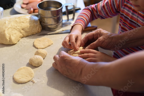 Grandmother helps her granddaughter to make a pie from homemade dough.