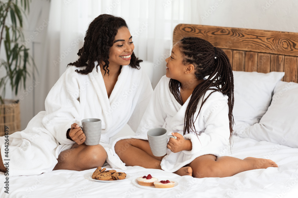 Happy African American Mom And Daughter In Bathrobes Having Snacks In Bed Happy African American Mom And Daughter In Bathrobes Having Snacks In Bed