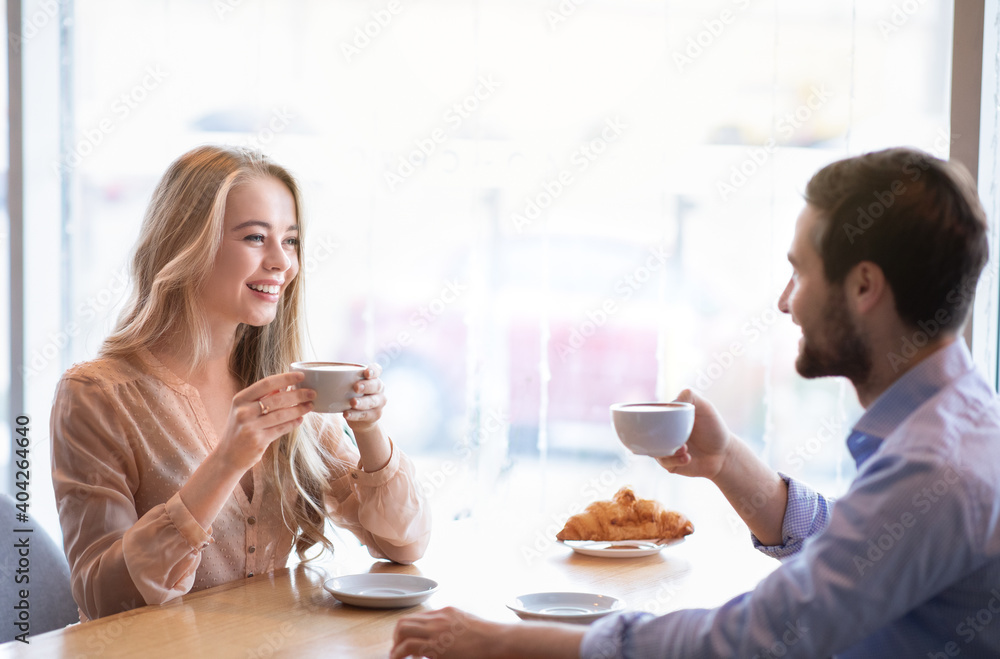 Portrait of affectionate couple sitting at table in city cafe, drinking aromatic coffee, enjoying each other's company Portrait of affectionate couple sitting at table in city cafe, drinking aromatic coffee, enjoying each other's company