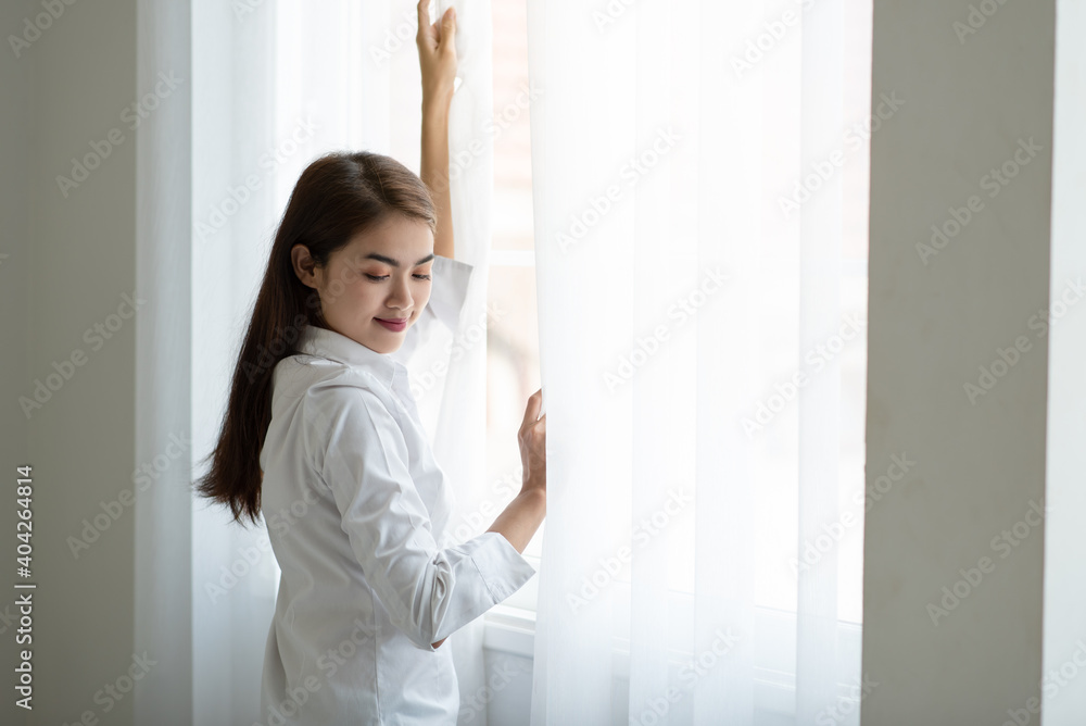 Young Asian woman opening the curtain in the morning after wake up Young Asian woman opening the curtain in the morning after wake up