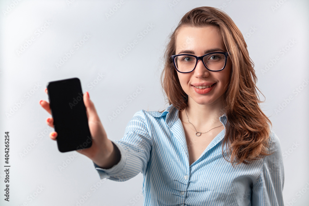 beautiful girl in a blue shirt and glasses shows the phone screen on a white background. isolated