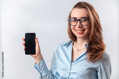 beautiful girl in a blue shirt and glasses shows the phone screen on a white background. isolated