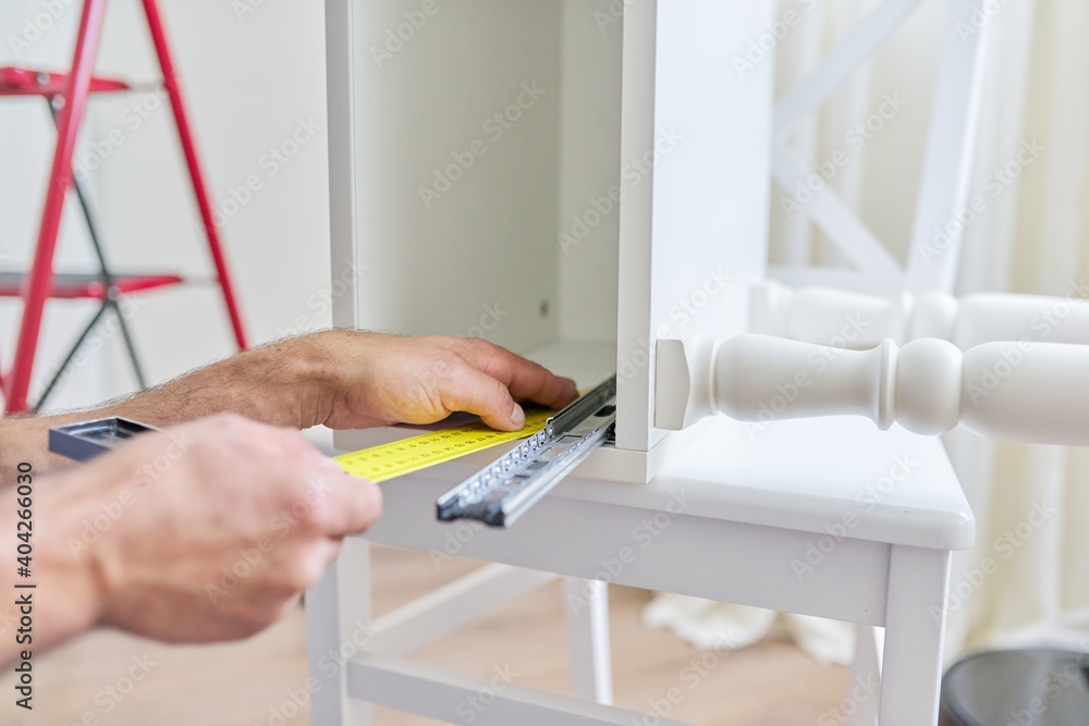 Assembly of wooden white bedside table at home, closeup of a worker's hand