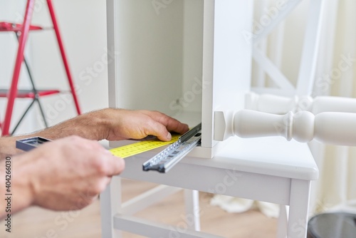 Assembly of wooden white bedside table at home, closeup of a worker's hand