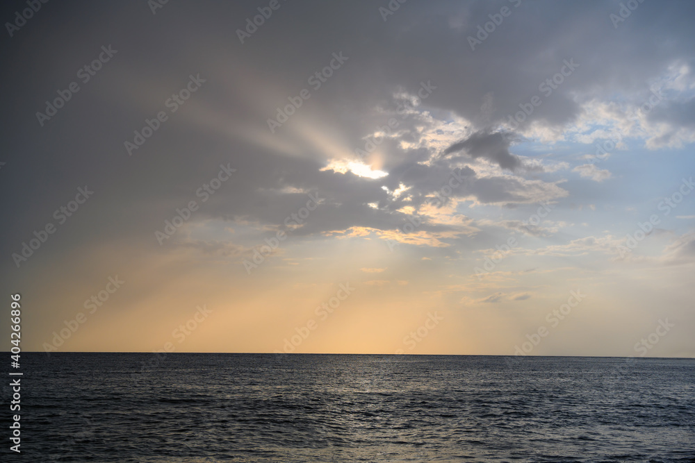 sunset over the sea. the sun descends, painting the gray sky with sunset yellow colors. rays of the sun shoot out of a hole in thick clouds, touching the rough surface of the water. autumn evening