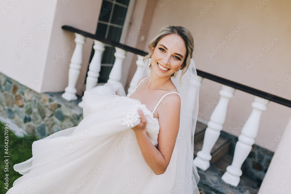 A beautiful and smiling blonde bride in a white lace dress is spinning and dancing in the park against the backdrop of the hotel in nature. Wedding portrait of a cute, emotional girl. A beautiful and smiling blonde bride in a white lace dress is spinning and dancing in the park against the backdrop of the hotel in nature. Wedding portrait of a cute, emotional girl.