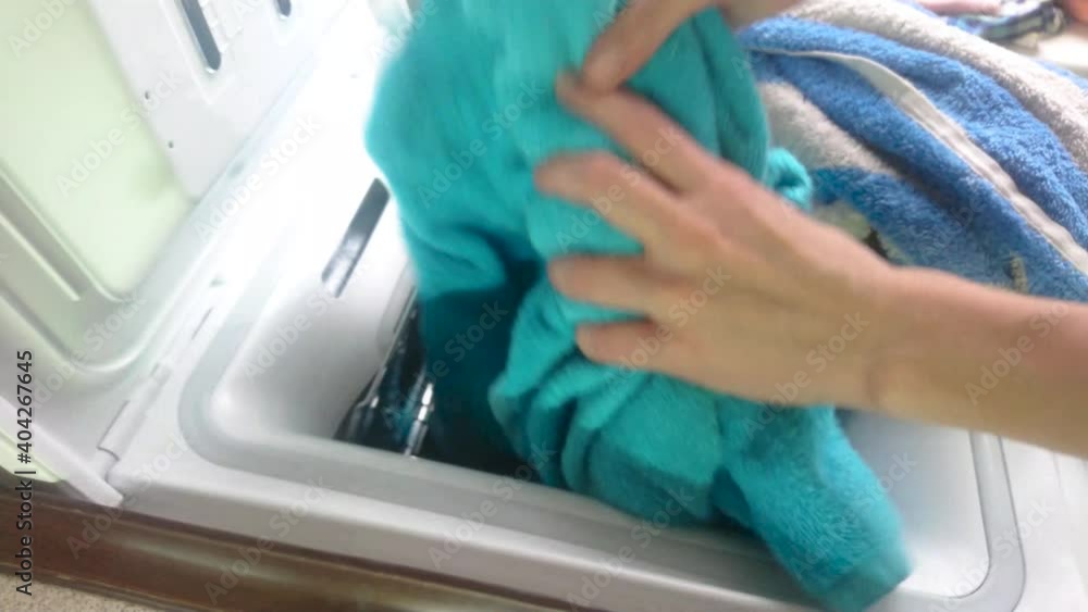 Woman loads dirty clothes into a vertical washing machine Woman loads dirty clothes into a vertical washing machine