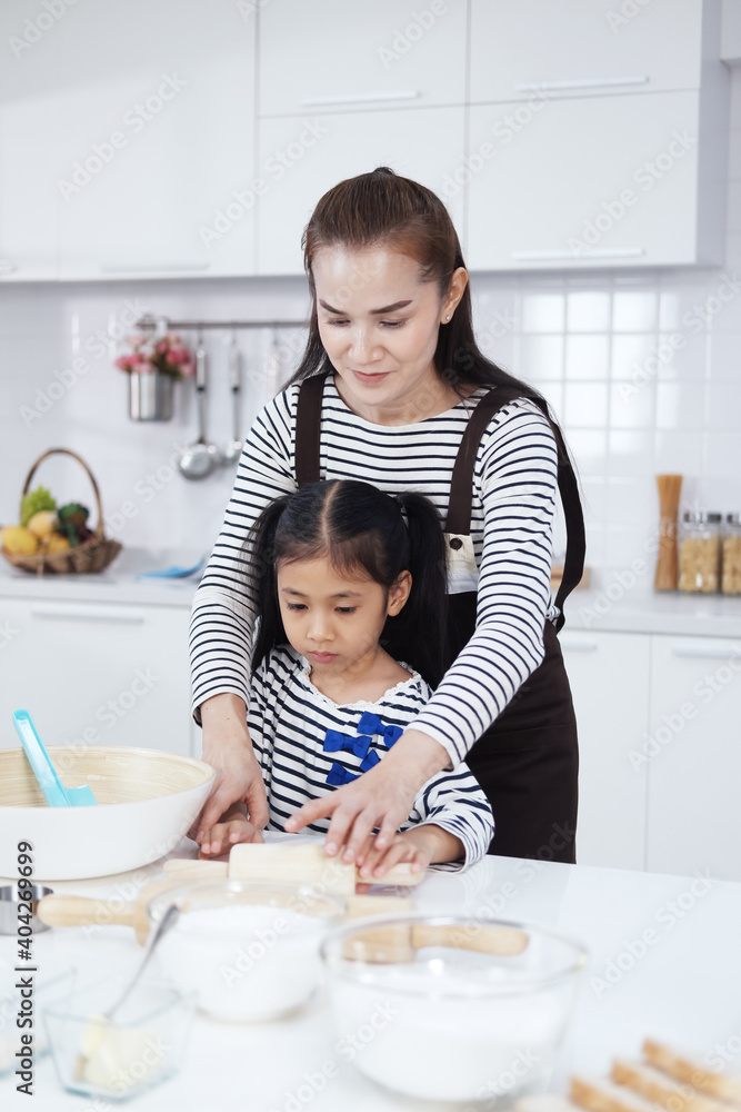 Smiling Asian mother and little asian girl child is Kneading the dough for baking bakery on wooden table together in kitchen. Homemade pastry for bread. Family love and Homeschool Concept. Smiling Asian mother and little asian girl child is Kneading the dough for baking bakery on wooden table together in kitchen. Homemade pastry for bread. Family love and Homeschool Concept.