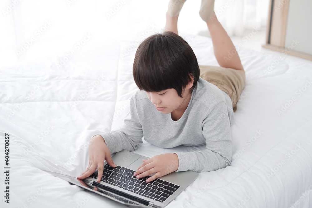 Smiling Asian little boy is studying and doing homework with laptop in bedroom. Homeschool and quarantine during Covid-19 virus epidemic concept. Distance Learning Online Education Smiling Asian little boy is studying and doing homework with laptop in bedroom. Homeschool and quarantine during Covid-19 virus epidemic concept. Distance Learning Online Education