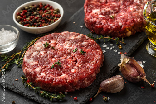 Fresh raw minced meat beef burgers patties on black slate board with spices and herbs for cooking on black background