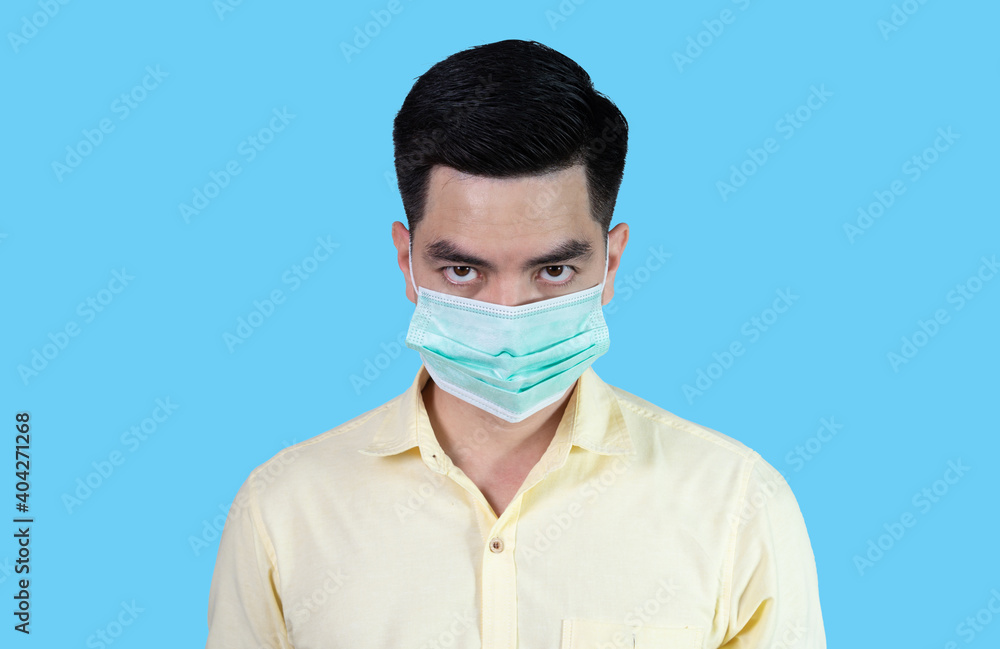 Close up COVID-19 Coronavirus portrait handsome young asian man wearing yellow shirt and sneezing mask protection from covid 19 isolated on blue background in studio. Asian man people. Close up COVID-19 Coronavirus portrait handsome young asian man wearing yellow shirt and sneezing mask protection from covid 19 isolated on blue background in studio. Asian man people.