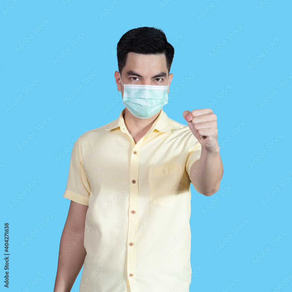 FIGHT! COVID-19 Coronavirus portrait handsome young asian .man wearing yellow shirt and mask protection from covid 19 isolated on blue background in studio. Asian man people. COVID-19 concept. FIGHT! COVID-19 Coronavirus portrait handsome young asian .man wearing yellow shirt and mask protection from covid 19 isolated on blue background in studio. Asian man people. COVID-19 concept.