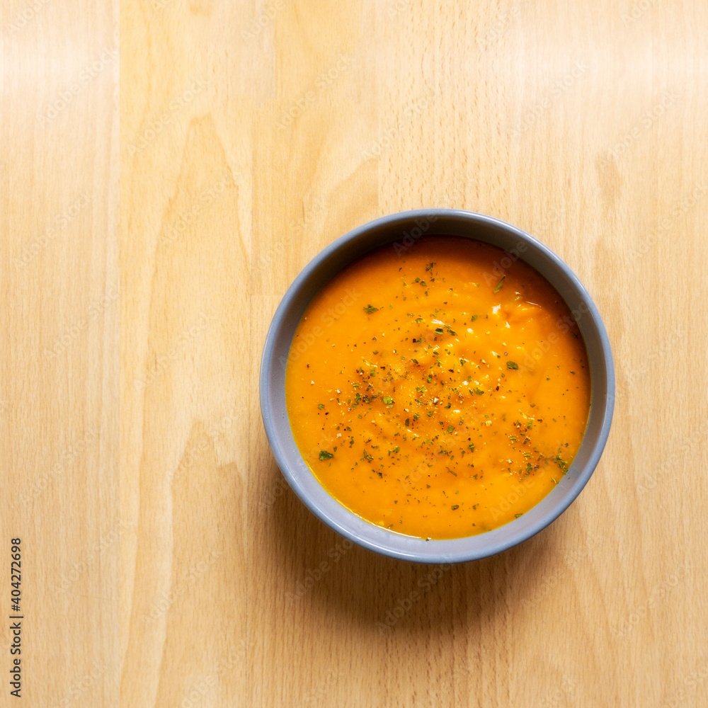Creamy pumpkin soup with chopped parsley and thyme herb, cream and pumpkin with pepper served in gray bowl on wooden table background. top view Creamy pumpkin soup with chopped parsley and thyme herb, cream and pumpkin with pepper served in gray bowl on wooden table background. top view