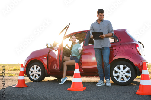 Instructor with clipboard near car and his student outdoors. Driving school exam © New Africa