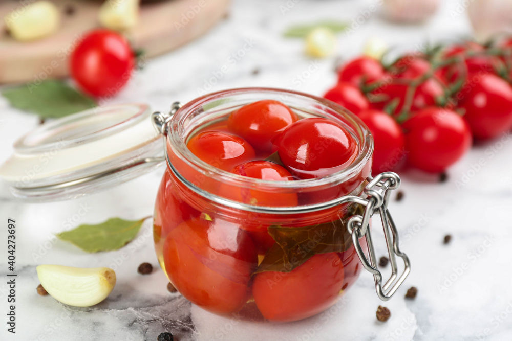 Glass jar of pickled cherry tomatoes and ingredients on white marble table, closeup Glass jar of pickled cherry tomatoes and ingredients on white marble table, closeup
