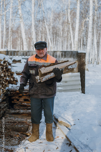 An elderly man collects firewood in a Russian village in winter