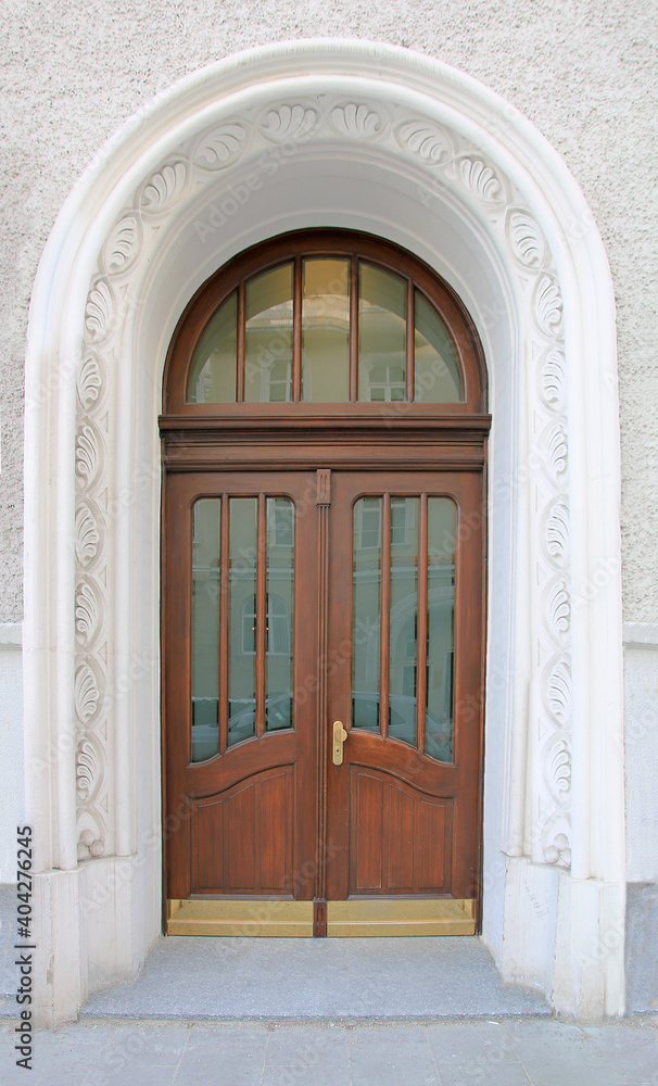 wooden door with glass and arched window, framed with stucco ornament. historic house entrance