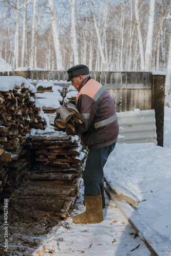 An elderly man collects firewood in a Russian village in winter