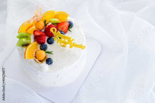 white cream cake with happy new year and topped with orange, strawberry, blueberry and Cape Gooseberry