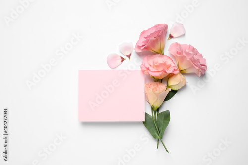 Beautiful Eustoma flowers and blank card on white background, flat lay. Space for text