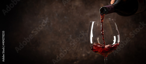 Fotografie, Tablou Pouring red wine into the glass against rustic dark wooden background