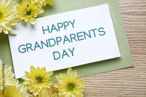 Beautiful yellow flowers and card with phrase Happy Grandparents Day on wooden background, flat lay