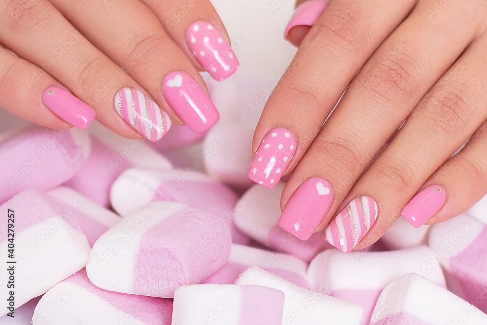 Female hands with pink manicure nails, hearts design on marshmallow background Female hands with pink manicure nails, hearts design on marshmallow background